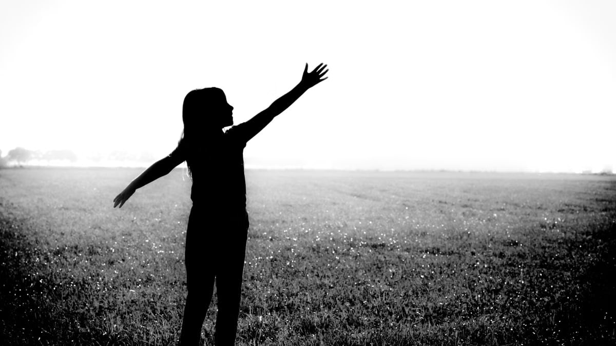 Black and white silhouette of a woman with arms outstretched in a field, symbolizing freedom and joy.